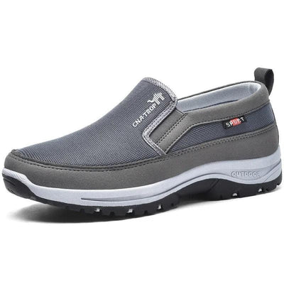 Harmaa hengittävä verkkokankainen slip on -kenkä leveällä pehmeällä pohjalla valkoisella taustalla